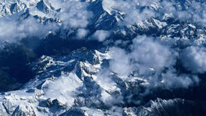 在廣闊的高山景觀中，積雪的山峰聳立於雲層之上。 — 唐人街 壁紙