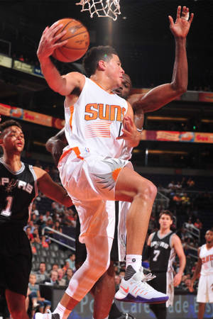 鳳凰城太陽隊籃球球員在場館中越過防守者灌籃。 — Devin Booker 壁紙