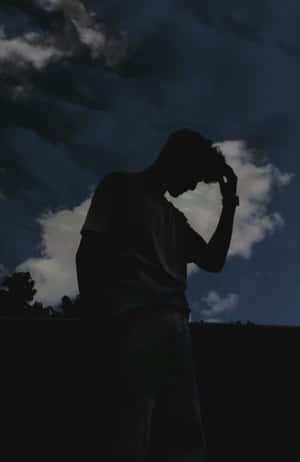 一個人的剪影，在黑暗的多雲天空下抱著頭。 — 剪影 壁紙