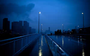 黃昏時分，一座被雨淋濕的城市橋樑，街燈倒映在濕漉漉的路面上。 — 藍色美學電腦 壁紙