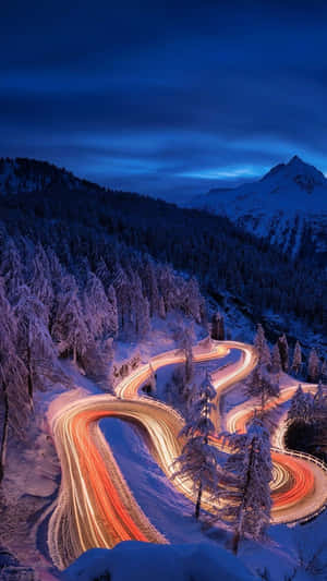 黃昏時分，蜿蜒的積雪山路，汽車的發光軌跡。 — 日落 壁紙