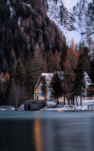 黃昏時湖邊的舒適小屋，雪山和溫暖燈光 — 冬季房屋 壁紙
