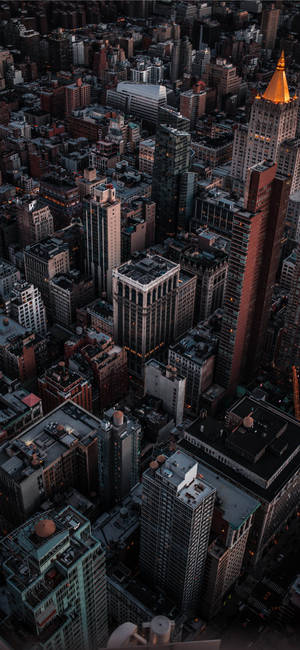 黃昏時分密集城市的鳥瞰圖，閃爍的燈光和高聳的建築物。 — iPhone 16 Plus 壁紙