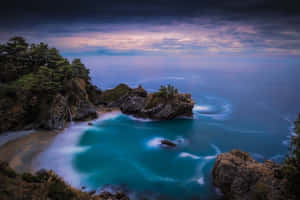 黃昏時分有藍綠色海水和瀑布的海岸小海灣 — MacBook Air 壁紙