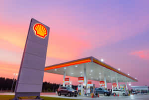 日落時分的Shell加油站，汽車在發光的燈光下加油。 — 3:2 壁紙