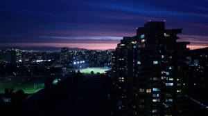 黃昏天空下，燈火通明的建築物和運動場的夜景 — 城市 壁紙