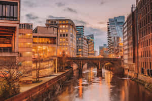 黃昏時分的城市河流景觀，建築物的燈光在水面上閃爍反射。 — 英格蘭 壁紙