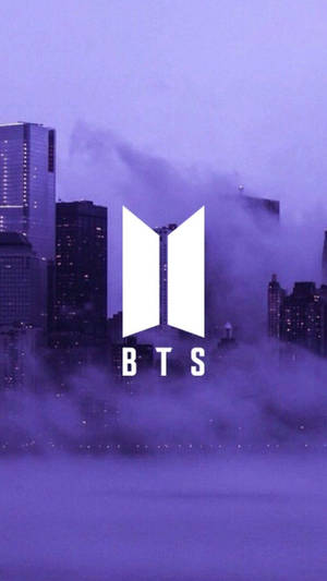BTS標誌在霧氣瀰漫的紫色城市天際線上方。 — BTS 紫色美學 壁紙
