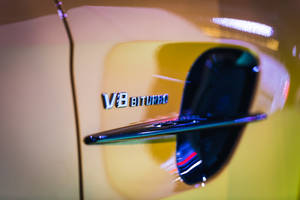 黃色車的V8 BITURBO徽章特寫，帶有霓虹反射。 — 賓士 AMG 壁紙