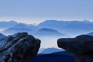 黎明時分，薄霧籠罩的山巒，以崎嶇岩石為框 — 山景 壁紙