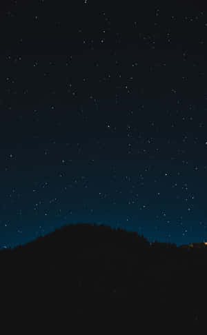黑暗森林山丘上方的星空夜空與遠方燈光。 — 簡約 壁紙
