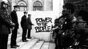 警察站在抗議者對面，附近塗鴉寫著power to the people。 — 黑豹 壁紙