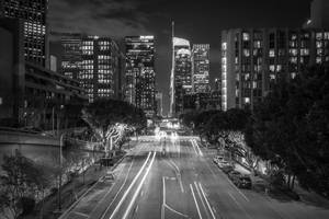 夜間城市街道，高樓之間有移動汽車的光跡。 — 洛杉磯 壁紙