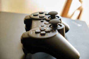 黑色Sony PlayStation 3手把放置在黑暗表面，搭配柔和燈光。 — PS3 壁紙