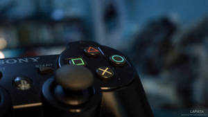 黑色PlayStation手把的特寫，帶有發光按鈕。 — PS3 壁紙