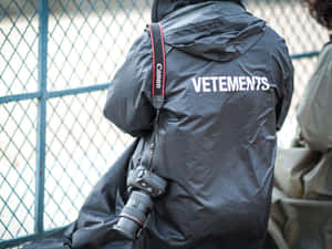 穿著黑色Vetements外套的人，肩上掛著Canon相機。 — Vetements 壁紙