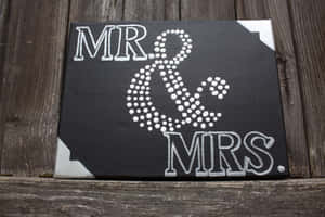 黑色畫布上印有白色 'MR & MRS' 文字及圓點&符號，木質表面。 — 3:2 壁紙