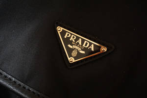黑色布料上帶金色邊框和縫線的Prada標誌貼章。 — Prada 壁紙