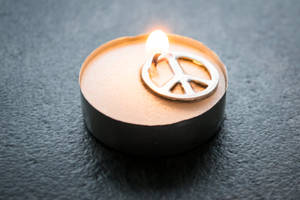 在深色石頭表面上燃燒的蠟燭，帶有和平符號設計。 — 蠟燭 壁紙